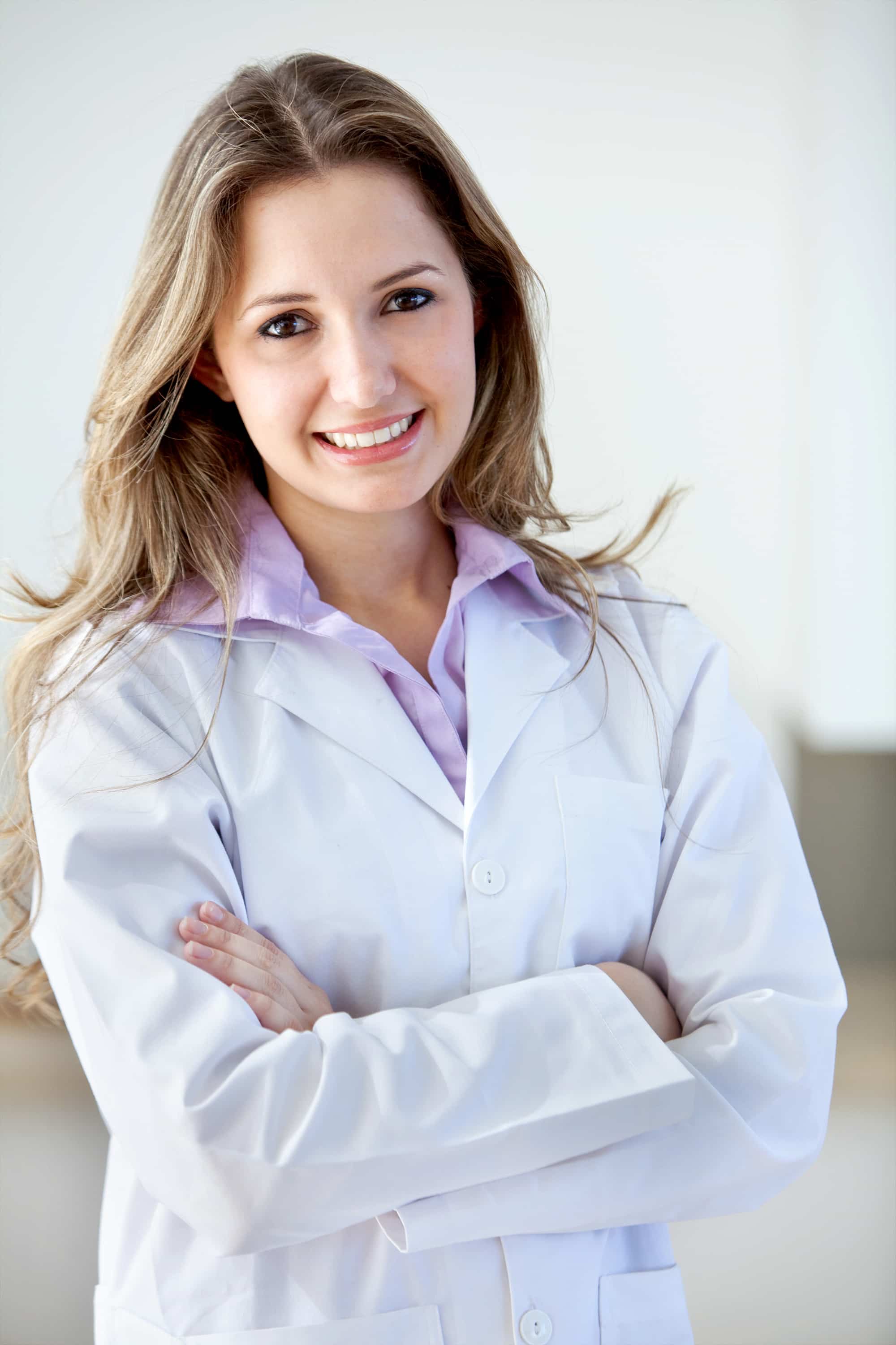A practitioner in a white coat, smiling with her arms folded.